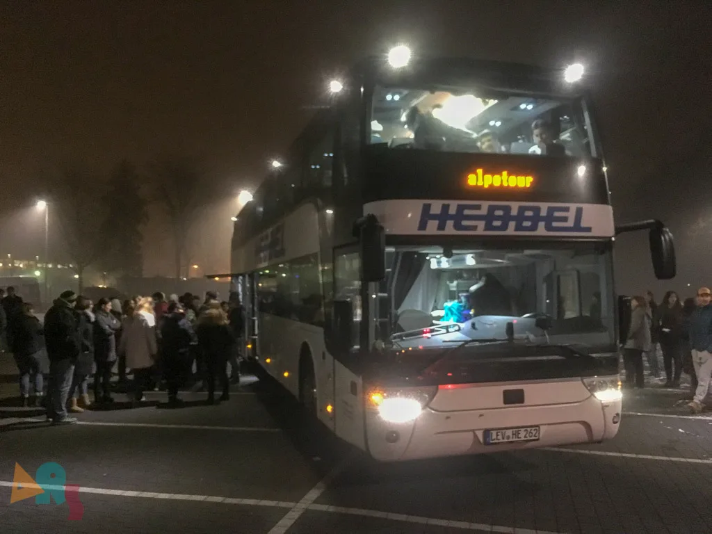 Reisebus steht abends im Schneefall vor der Gruppe.